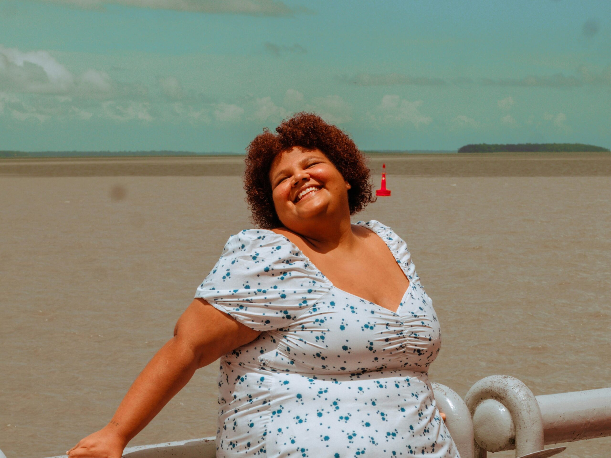 Smiling woman in white and blue dress in front of beach.